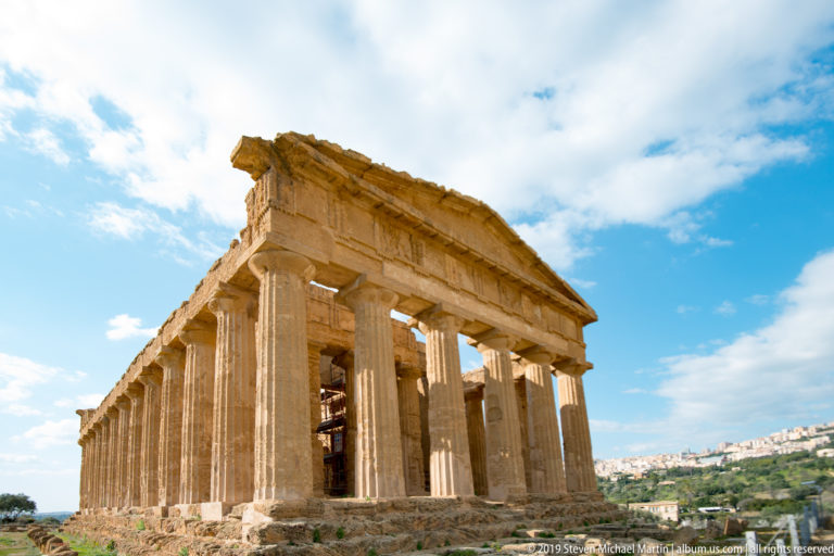 Low oblique view of the Temple of Concordia showing front columns and the long side colonnade beneath a bright sky.