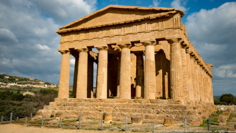 Three-quarter view of the intact Temple of Concordia with six-column façade, side colonnade, pediment, and stone platform.