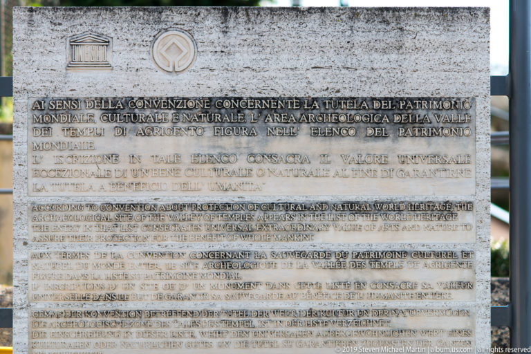 Stone plaque with UNESCO emblem and multilingual text commemorating the World Heritage status of Agrigento's archaeological area.