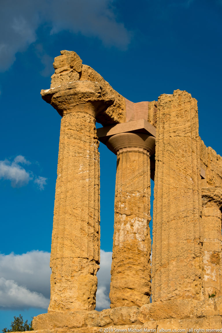 Close view of weathered Doric columns and entablature blocks in golden stone against a deep blue sky.
