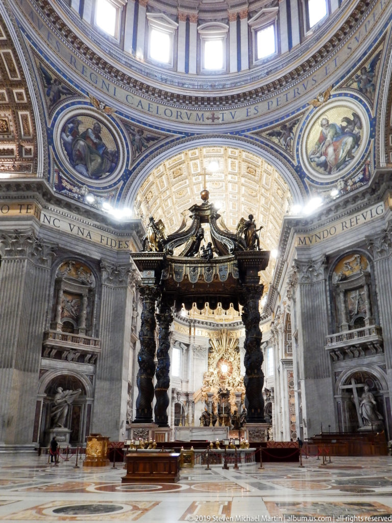 Frontal view of Bernini’s baldachin with twisted bronze columns, papal altar, and glowing apse visible through the canopy.