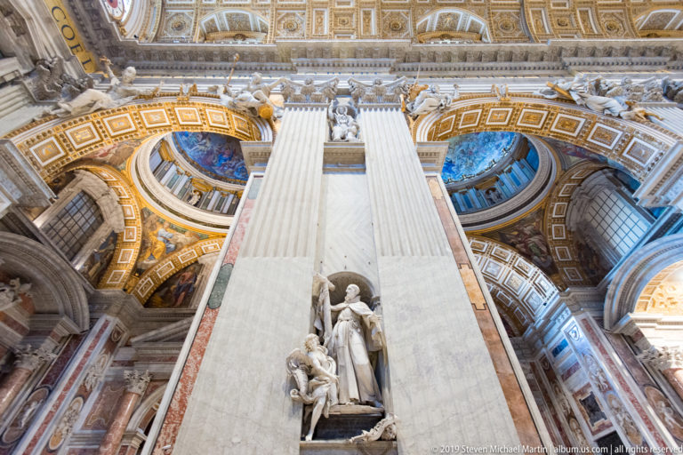 Low-angle view of a massive pale crossing pier with a sculptural niche below and gilded arches and blue mosaics overhead.