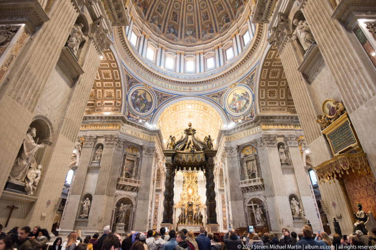 Visitors in the foreground beneath Saint Peter’s dome, with giant piers and Bernini’s baldachin centered in the distance.