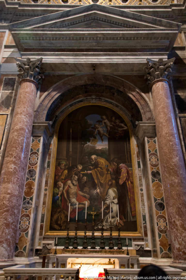 Side altar framed by red marble columns, with a large religious painting above candles and a polychrome marble architectural surround.