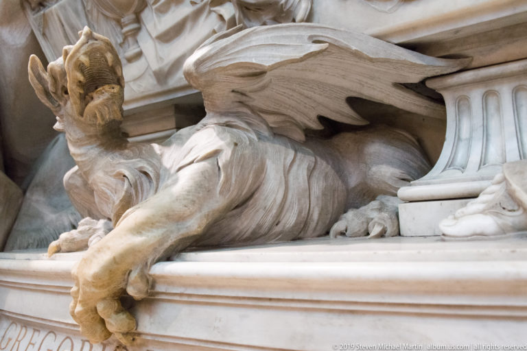 Close view of a carved marble dragon with spread layered wings projecting from the base of an architectural monument.