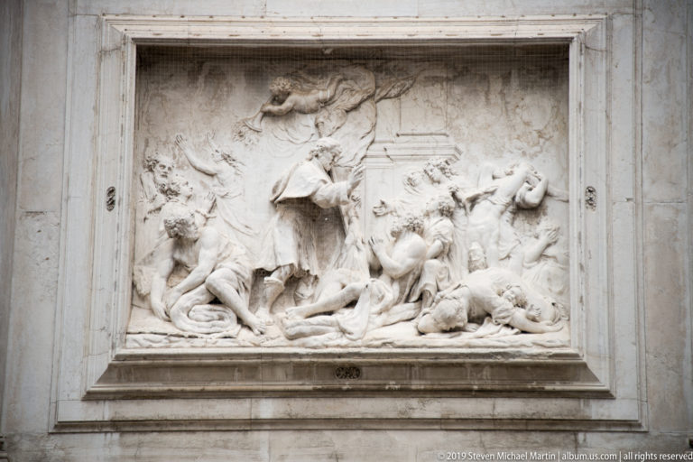 Large rectangular marble relief with crowded human and animal figures carved in deep, shadowed relief within a plain stone frame.