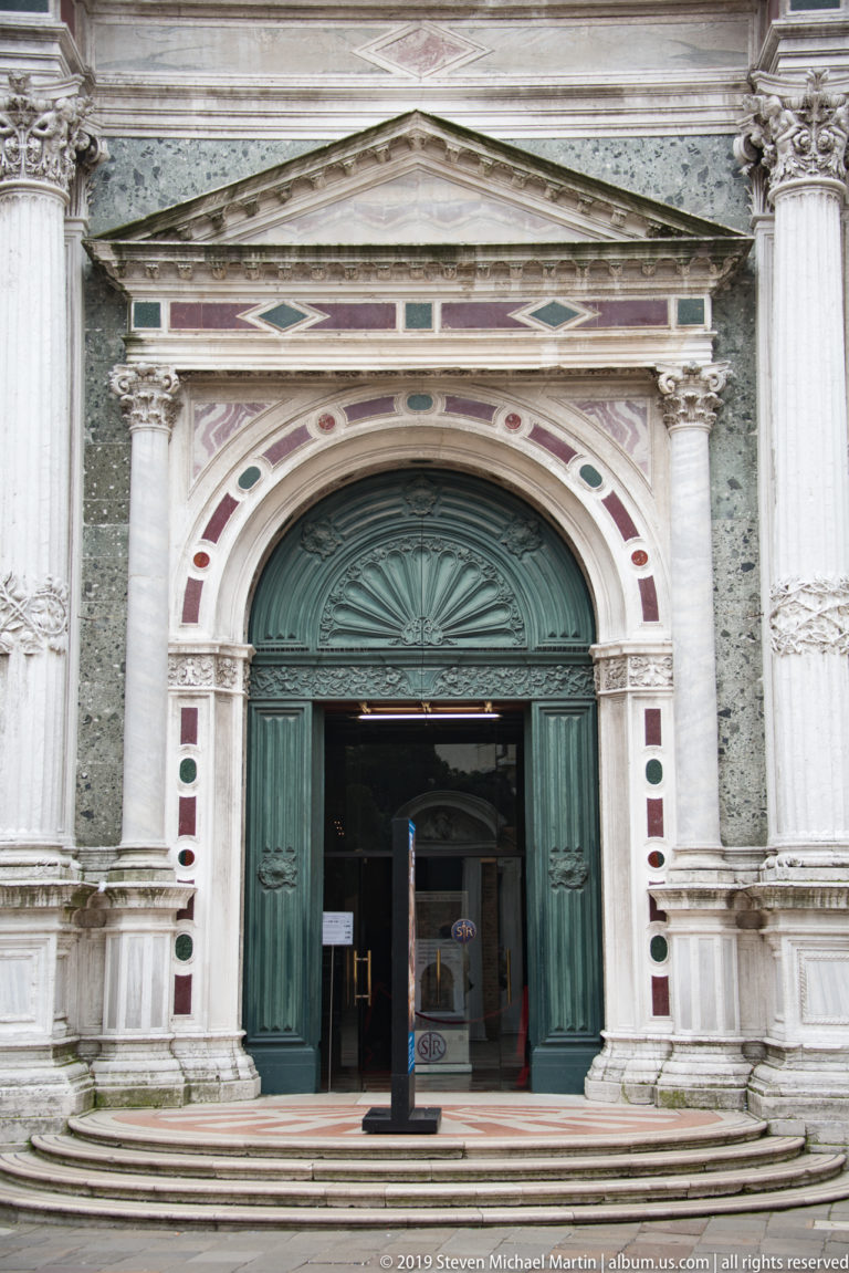 Large arched green church doorway framed by pale carved stone, columns, and red-and-green marble decorative insets.