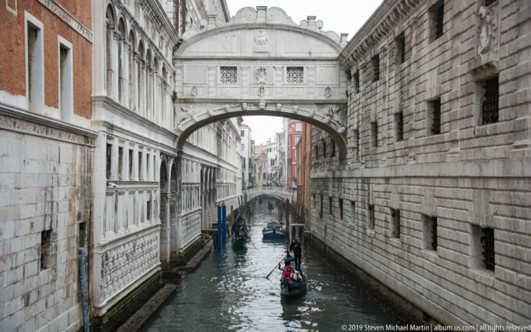 Bridge of Sighs crossing a narrow canal above gondolas between pale palace walls and rusticated stone masonry.