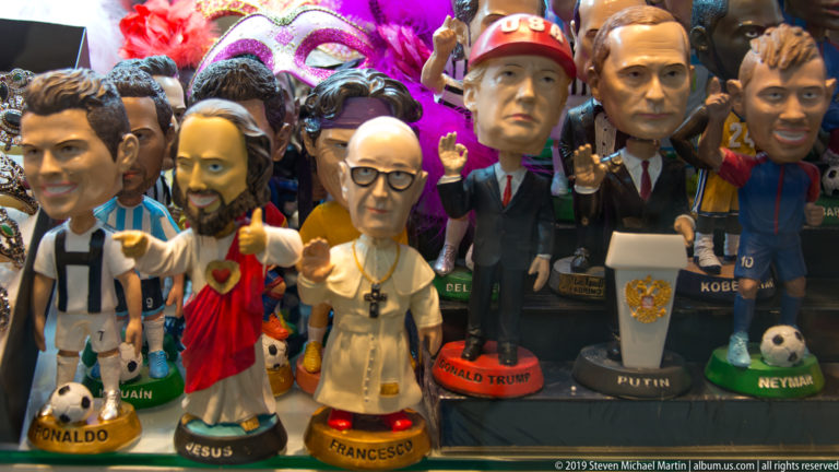Rows of caricature figurines labeled Ronaldo, Jesus, Francesco, Donald Trump, Putin, and Neymar in a colorful souvenir display.