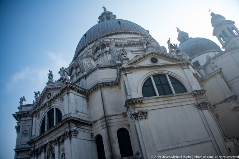 Low oblique view of Santa Maria della Salute showing its large dome, sculpted stone façades, windows, and smaller dome beyond.