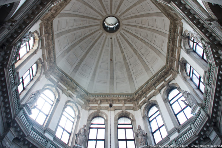 Upward view inside a pale ribbed dome with central oculus and a ring of tall windows around the drum.