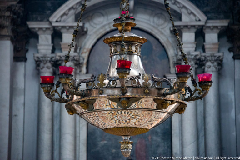Ornate hanging church lamp with red glass cups, pierced metalwork, patterned glass bowl, chains, and pendant.