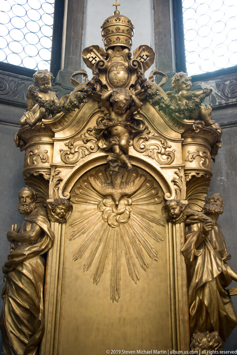Gilded Baroque ornament with papal tiara, crossed keys, rays, scrolling foliage, and small sculpted figures.