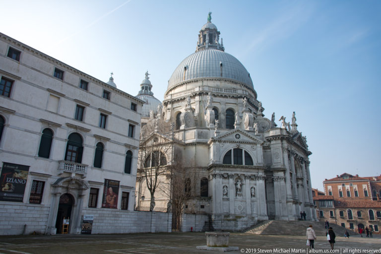 White stone Basilica di Santa Maria della Salute with its large dome and sculpted exterior seen from the campo.