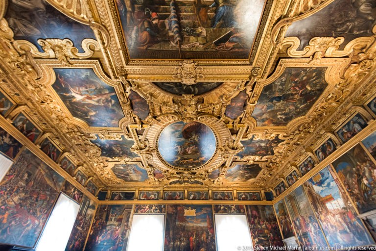 Upward interior view with a central oval ceiling painting, gilded frames, surrounding narrative panels, and large wall paintings below.