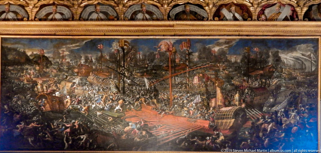 Wide historical battle painting with dense armies, banners, artillery, smoke, fortifications, and a mountainous landscape.