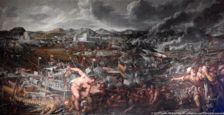 Large historical painting of a naval battle with warships, smoke, crowded troops, and foreground combatants beneath a dark sky.