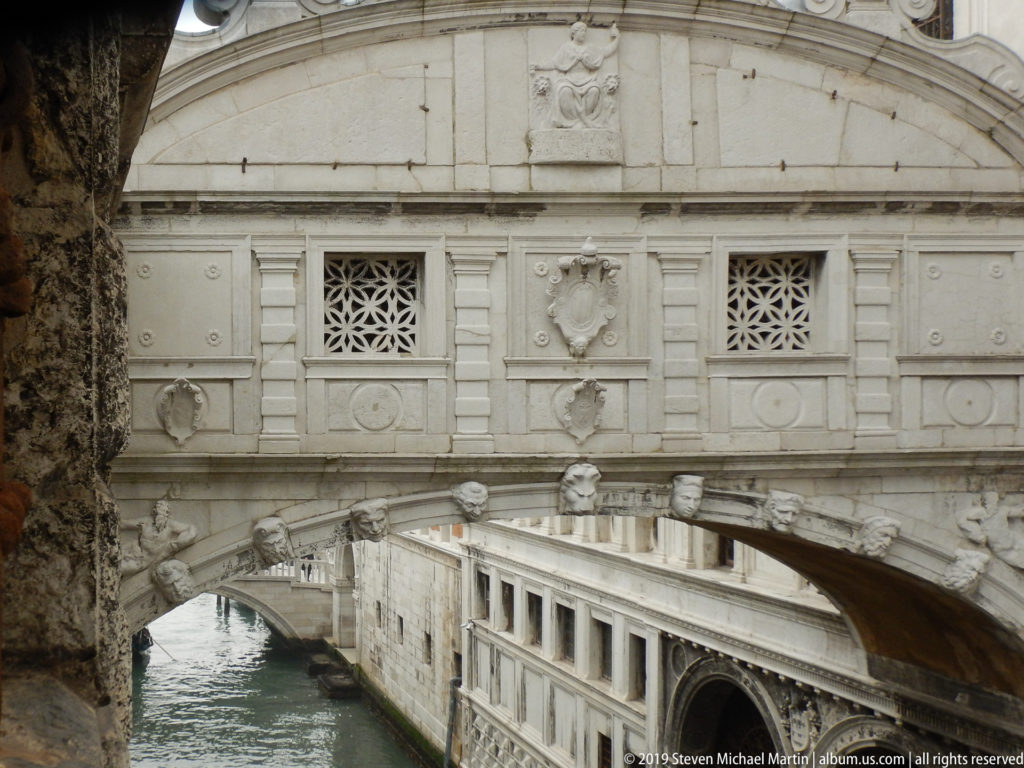 Bridge of Sighs spanning a canal beside the long pale stone façade of the historic prison wing.