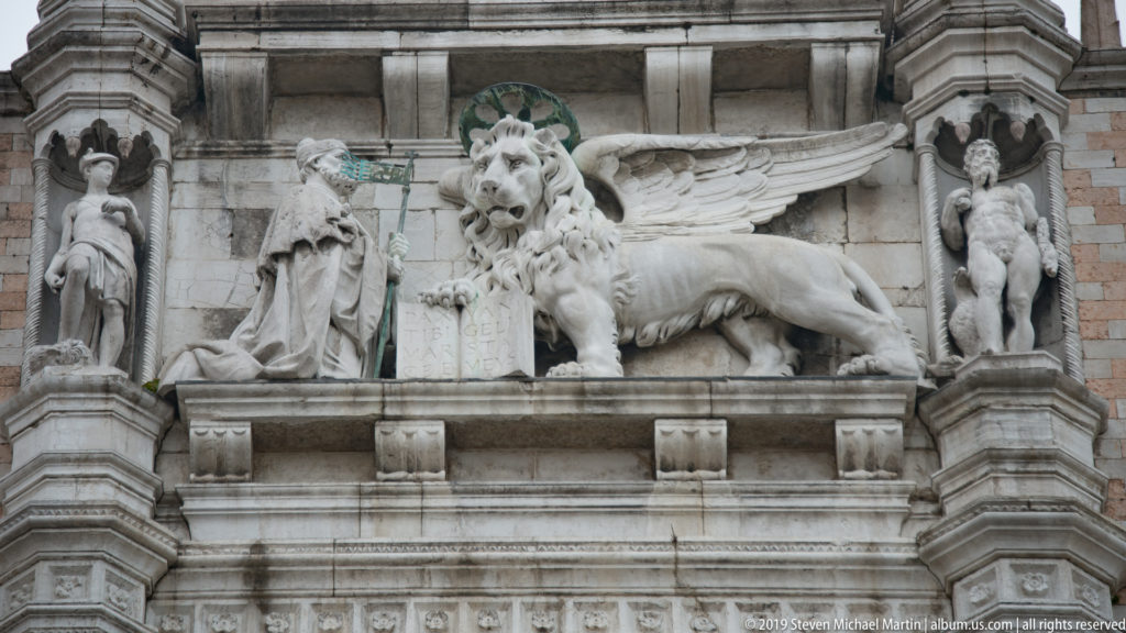 Stone relief of the winged Lion of Saint Mark between standing figures on the exterior of Palazzo Ducale.