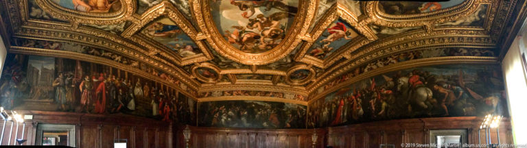 Corner of a ceremonial interior with long wall paintings, dark wood paneling, and an elaborate gilded painted ceiling.