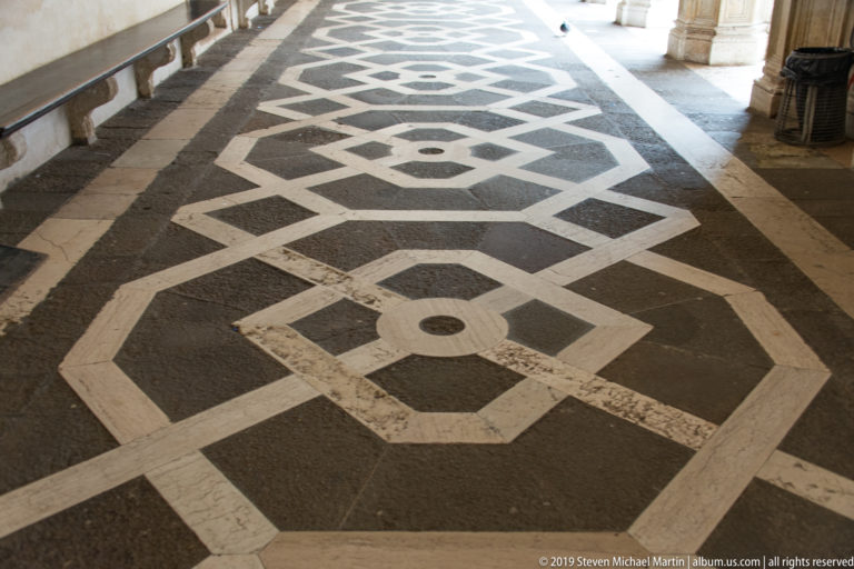 Black, white, and gray stone pavement arranged in repeating octagons, diamonds, and circular geometric motifs.