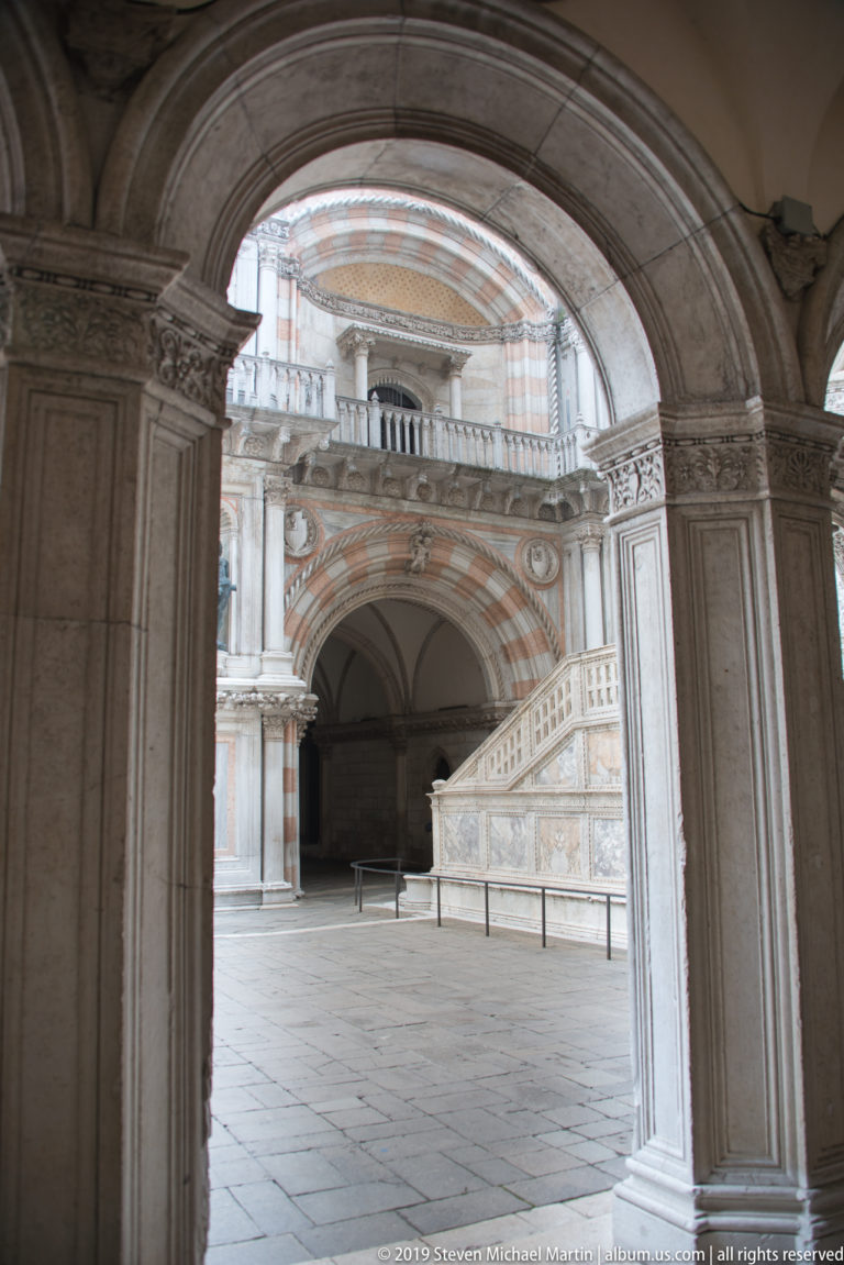 Large stone archway framing the courtyard and the lower flight of the Scala dei Giganti beyond.