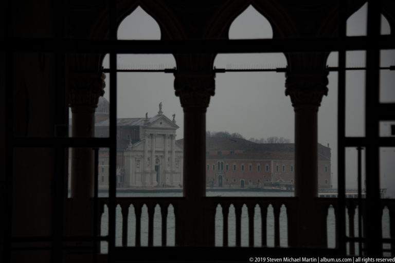 San Giorgio Maggiore across the lagoon, framed by silhouetted pointed arches and columns of the Palazzo Ducale.