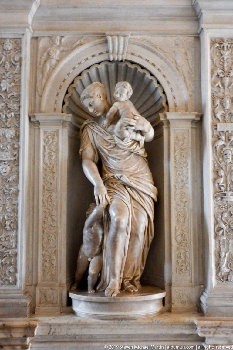 Two carved marble figures closely grouped in a scallop-shell niche with ornamental pilasters.