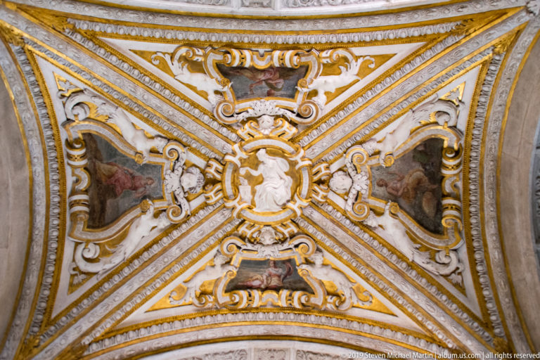 Gilded groin vault with painted panels, white stucco ornament, and a central oval medallion.