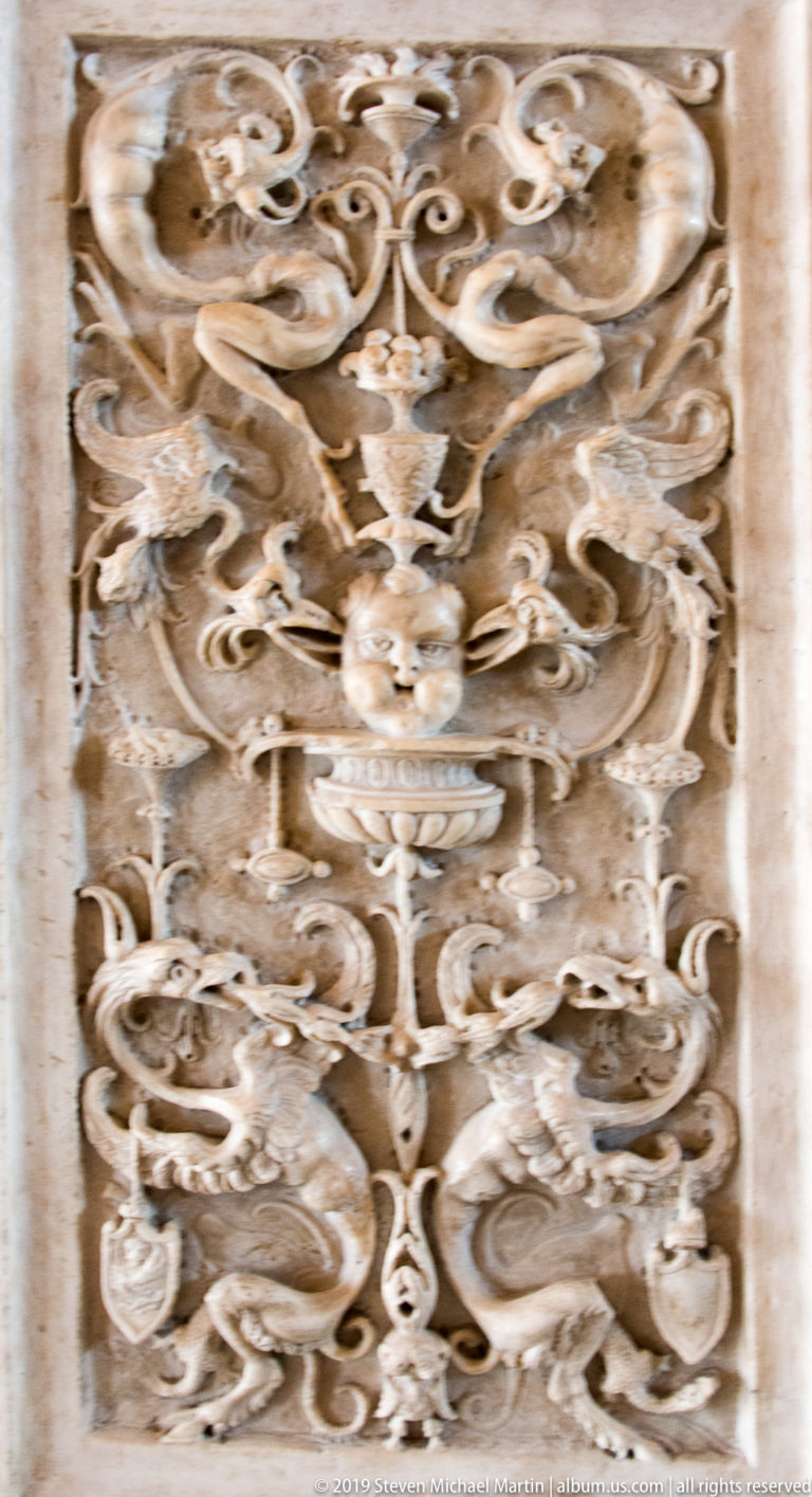 Close-up of pale ornamental relief filled with curling foliage, scrolls, masks, and small grotesque forms.
