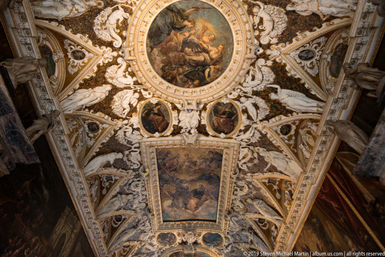 Vault section with a large circular painting above a rectangular canvas, surrounded by smaller medallions and white-and-gold stucco figures.