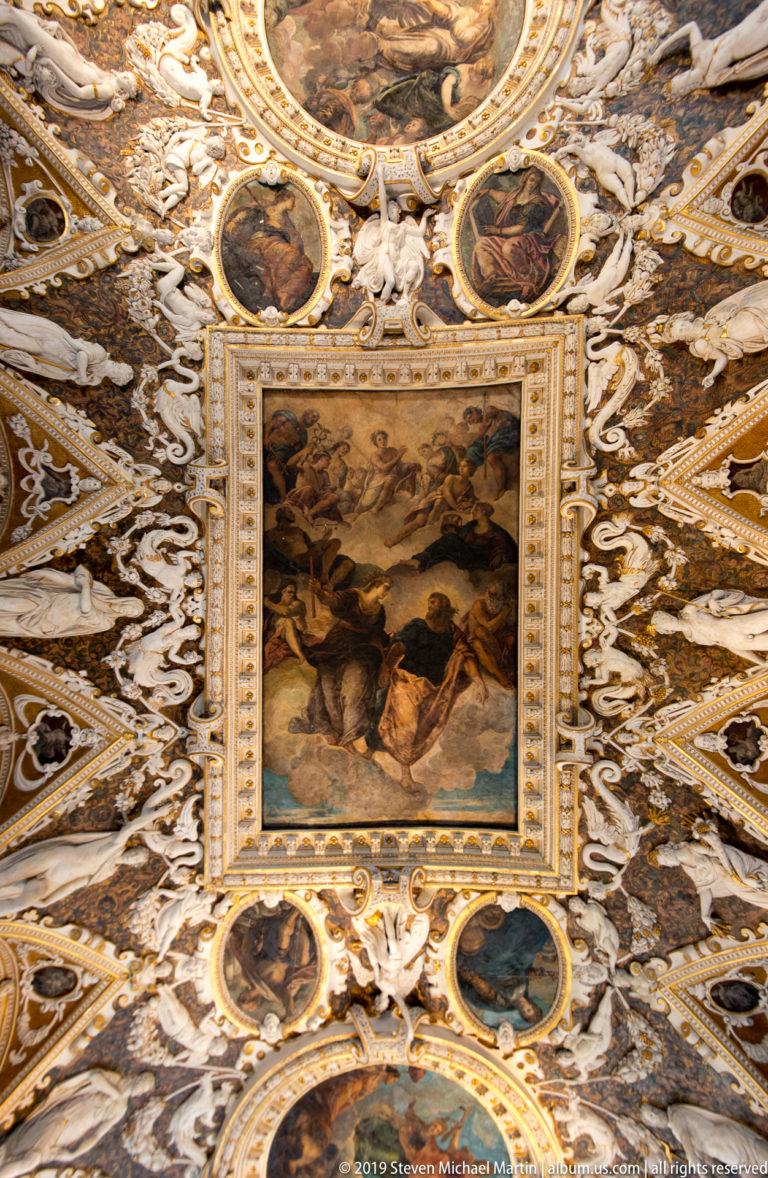 Rectangular multi-figure ceiling painting framed by white stucco figures, gold ribs, and smaller circular painted medallions.