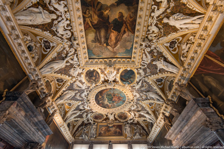 Long axial view of a richly painted and stuccoed vault extending toward a bright window at the far end.
