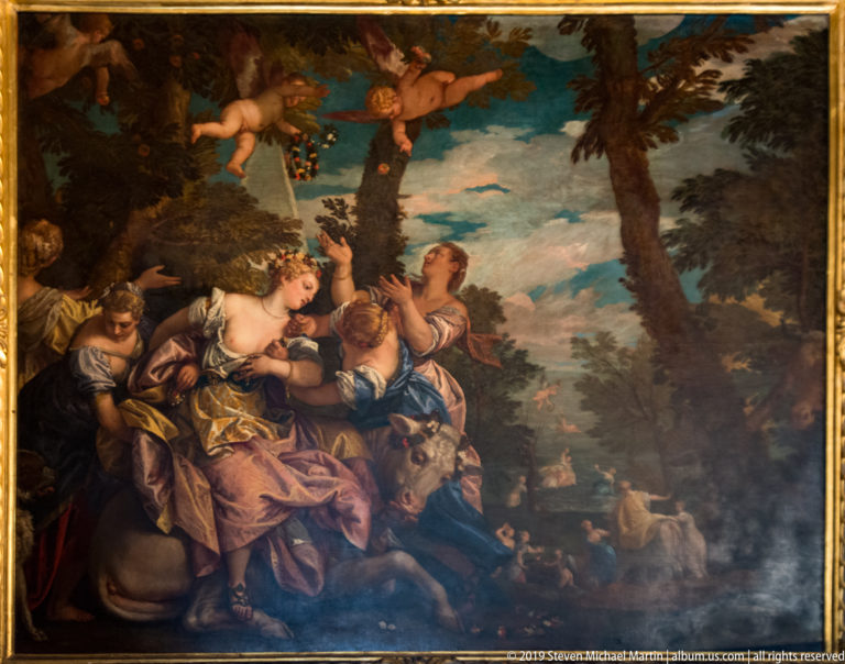 Mythological or allegorical painting with three women under trees, winged putti overhead, and a pastoral landscape in the distance.