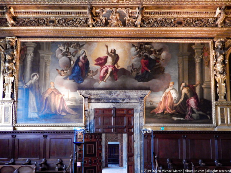 Large architectural wall painting with seated and standing figures above a real wooden doorway and dark paneling.