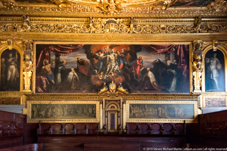 Large ceremonial painting over a central doorway, with two long monochrome panels and wooden benches below.