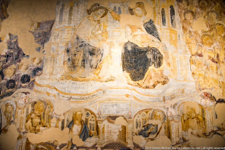 Faded fragmentary wall painting with architectural forms, small figures, arches, and extensive areas of pigment loss.
