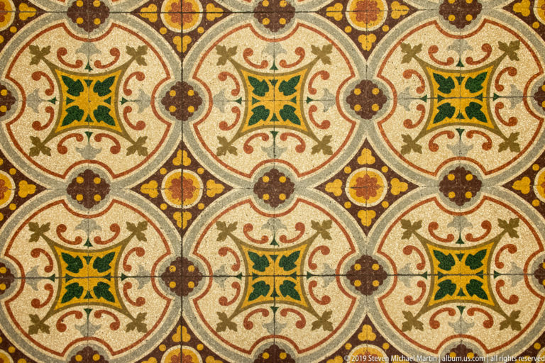 Polychrome floor with repeating interlocking circles, green-centered squares, ocher floral motifs, and red geometric outlines.