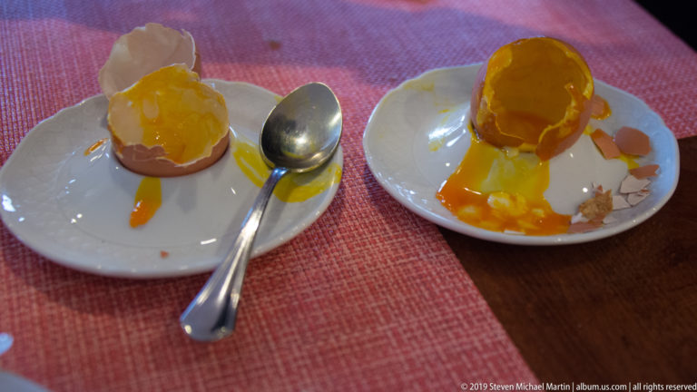 Two small opened dessert shells filled with orange-yellow custard or sauce on white plates beside a spoon.