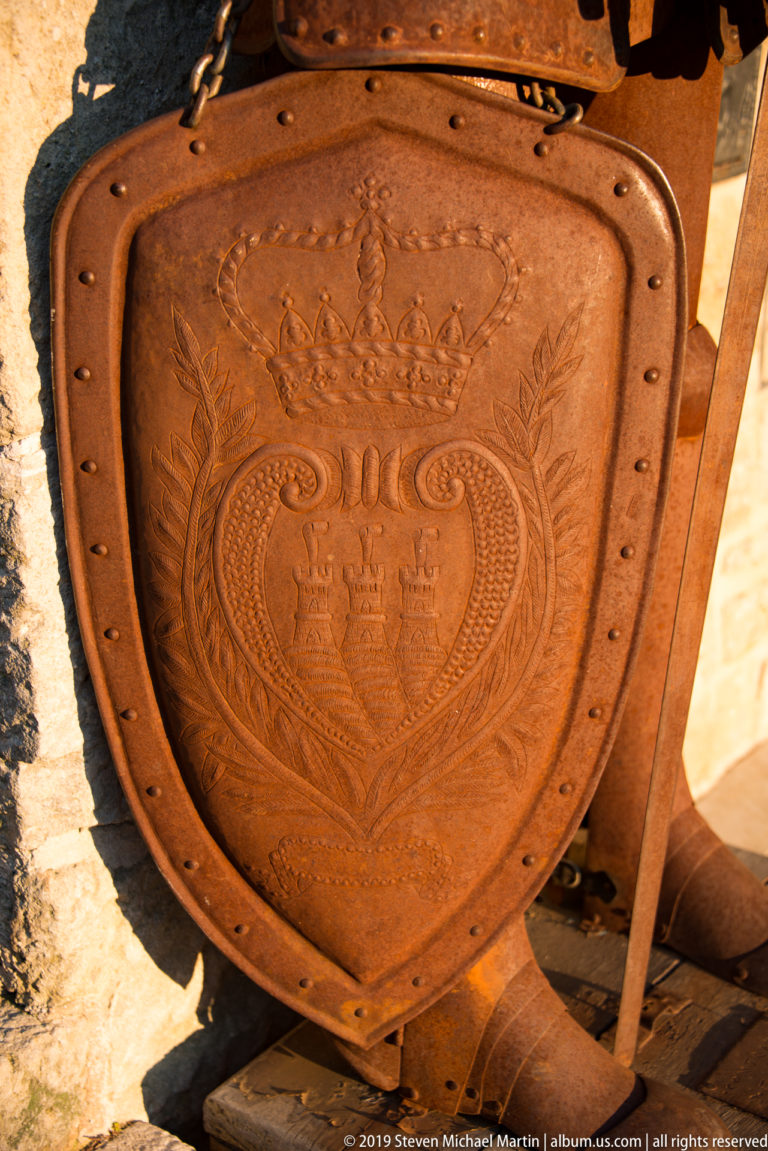 Rust-colored shield embossed with San Marino’s crowned three-tower emblem, scrolling ornament, and riveted border.