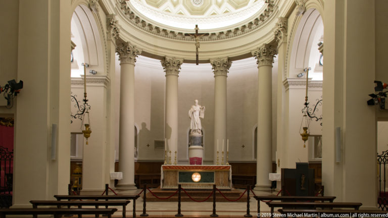 Wide sanctuary of the Basilica of Saint Marinus with Corinthian columns, high altar, and Adamo Tadolini’s Saint Marinus statue centered in the apse.