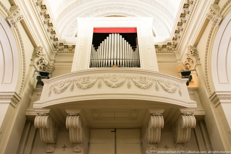 Giacomo Bazzani’s 1835 pipe organ with silver pipes in a white case above the decorated entrance gallery of the Basilica of Saint Marinus.