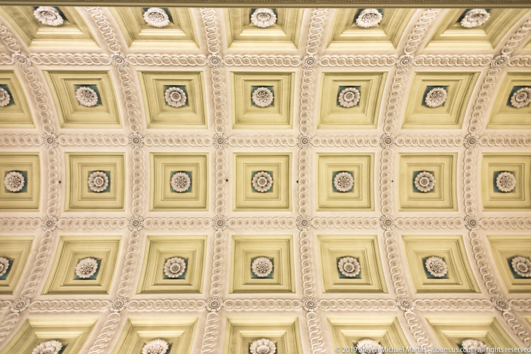Grid of cream-and-gold square ceiling coffers, each centered with a sculpted floral rosette and framed by beaded moldings.