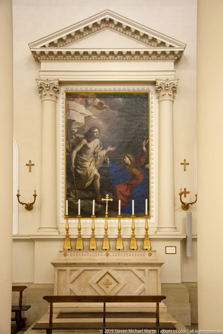 Classical side altar with dark religious painting of two figures above a row of gold candlesticks.