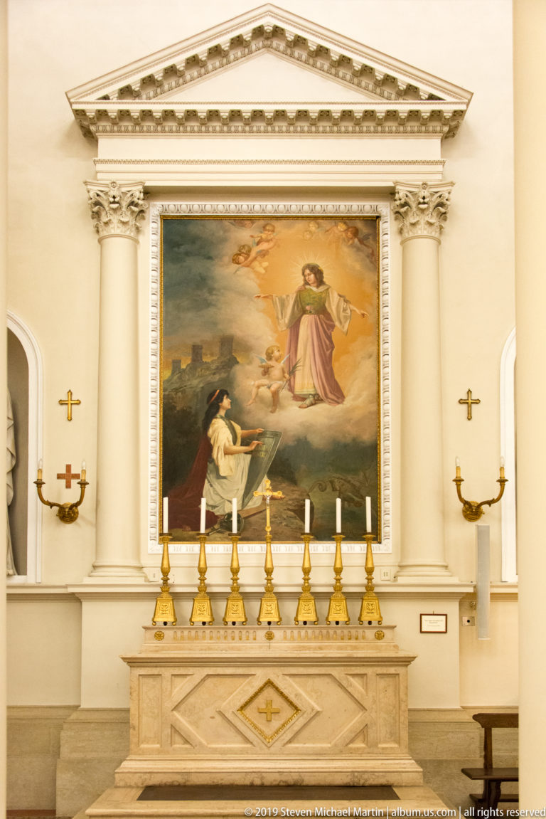 Side altar with a large religious painting of a standing figure above a kneeling figure, framed by columns and gold candlesticks.