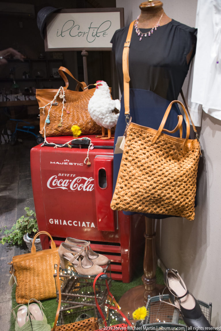 Handbags, shoes and a dark dress arranged around a red vintage Coca-Cola cooler in a shop display.