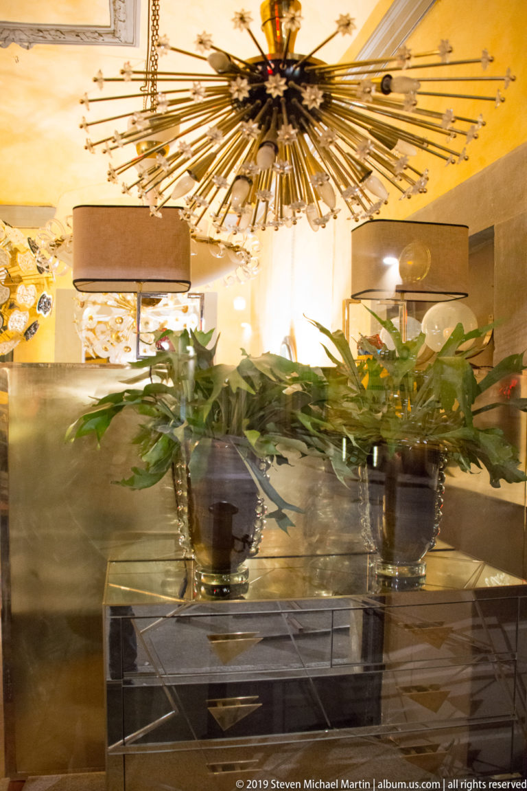 Large starburst chandelier above leafy plants on a mirrored console in a warmly lit interior.