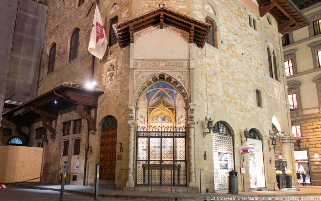 Stone exterior of Orsanmichele with projecting canopy, pointed doorway, and illuminated Gothic tabernacle at night.