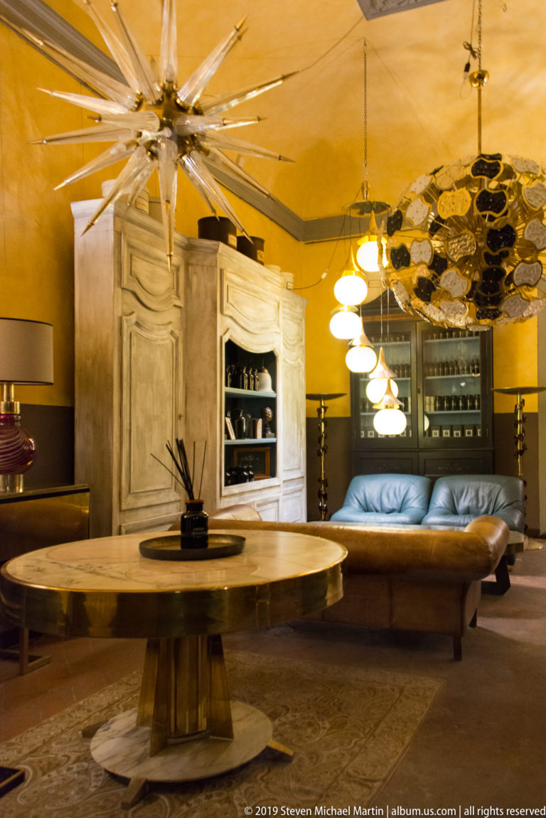 Round wooden table, leather sofa, pale cabinet and clustered pendant lights in a warmly lit furniture showroom.