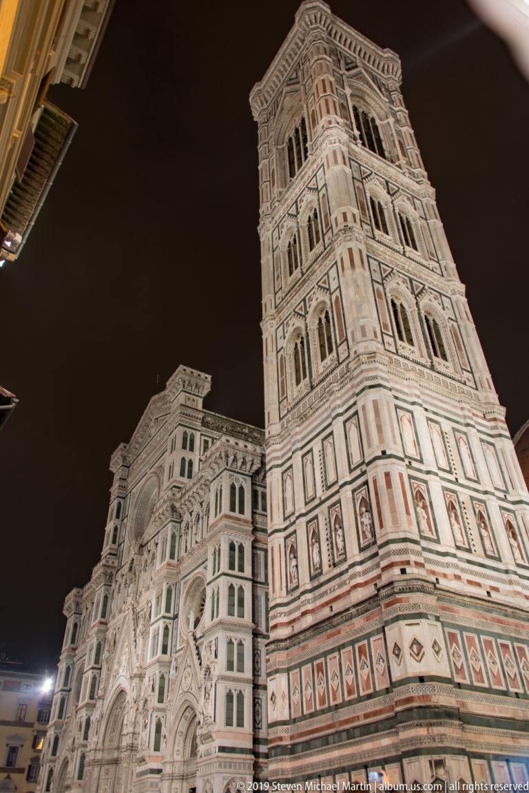 Low-angle nighttime view of Giotto’s Campanile towering above part of the Florence Cathedral façade.